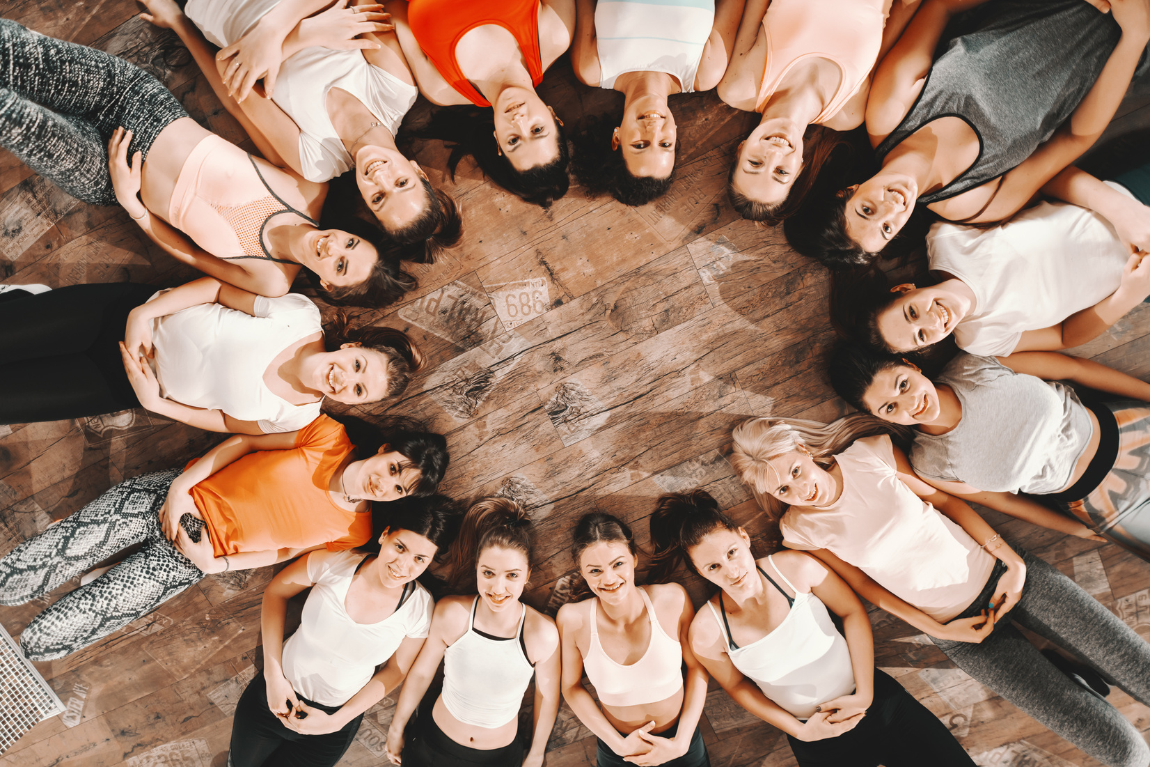 Top view of women lying down on the gym floor in circle.